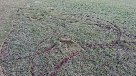 Muddy lines in turf can be seen going in all different directions including in a circle in the middle with several lines coming out of it.