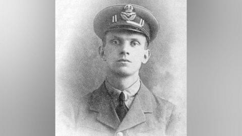 A black and white portrait photo of a young man. He has a Royal Air Force hat on, a jacket buttoned up and a shirt with a dark tie.