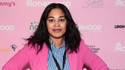 Ellisha Soanes looks at the camera, wearing a pink jacket in front of a branded backdrop.