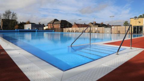 A deserted lido flanked by houses. Wide steps take swimmers into the water.