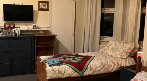 A single bed, TV, cabinet and toiletries in a cosy room. The head of the bed is inside a bay window.