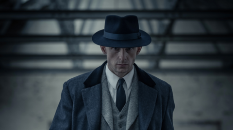 A Man in a 1950s suit walking with a serious expression on his face.