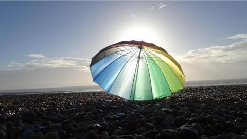 A multi-coloured umbrella on the beach with partly blue sky behind