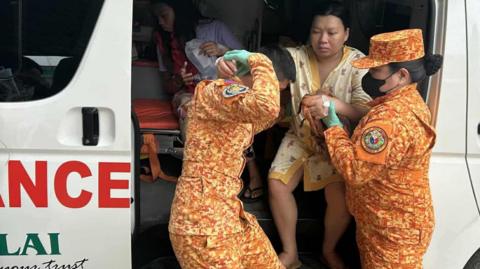 A woman is helped out of an ambulance by two members of the Philippines fire service   