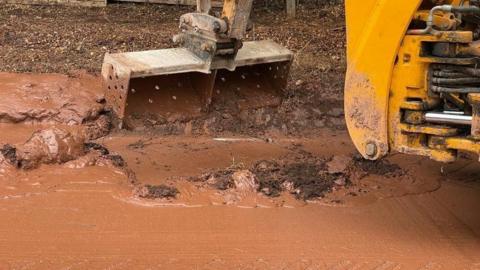 A close up of a yellow digger removing mud from the side of the A358. 