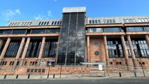 Newcastle Crown Court. It is a large imposing building with red bricks and columns and large dark windows.