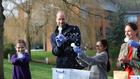 The Prince of Wales with local schoolchildren as they filter DNA samples through a syringe after extracting water from a local pond in order to see which species live in it