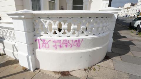 A white wall outside a house with the word "tax evasion" wrote in pink on it