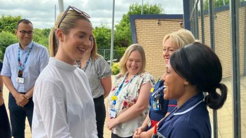 Rosie Wrighting with long blond hair and a white top talking to a nurse in uniform