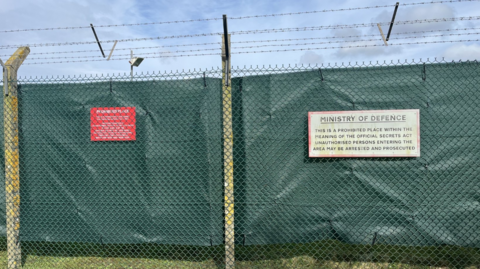 Green tarpaulin attached to a chain link fence with barbed wire running across the top