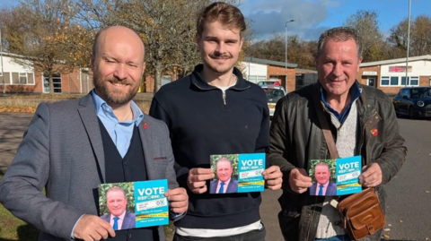 Three men holding Reform UK leaflets