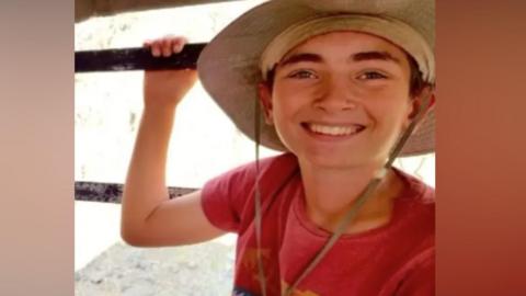 A young boy on holiday. He is smiling and wearing a big hat. 
