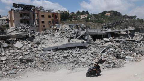 A man riding a motorcycle past destroyed buildings in the village of Mayfadoun, southern Lebanon (23 June 2026)