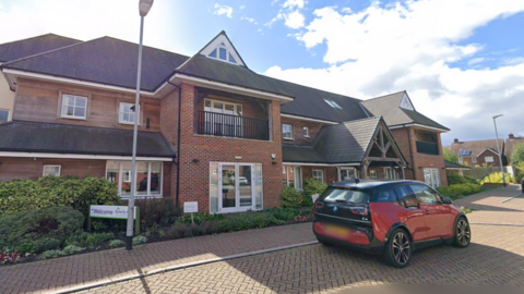 A hospice building with a red car parked outside.