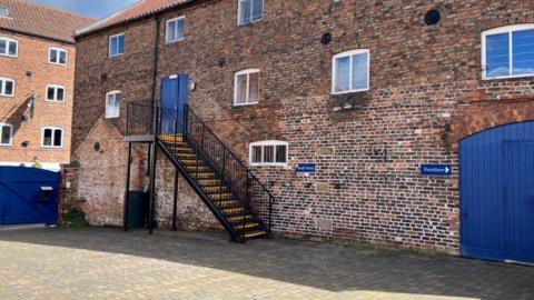 Three-storey building with access doors painted blue, and a black metal staircase leading to a first-floor door