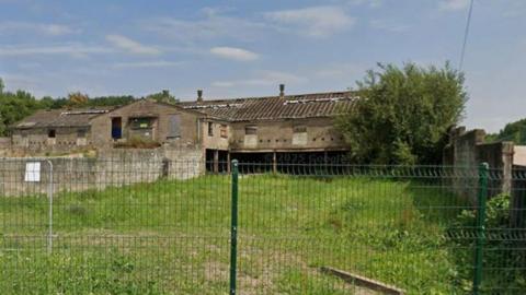 A derelict farm building with fences in front of it.