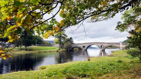 A view of Kenmore Bridge at the opening to Loch Tay which separates the lake from the river of the same name - as seen here from under autumnal trees.