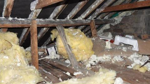 An attic space with wooden beams. There are two huge balls of insulation foam and the whole space is scattered with pieces of broken polystyrene. 