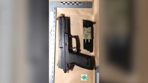 A black handgun on a wood counter top will a tape measure and police evidence labels