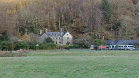 A large historic building sits in a national park. Minibuses can be seen parked to the side.