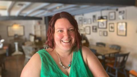 Woman with red hair wearing a green top and smiling