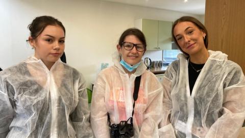 Three students from Nottingham College wearing personal protective equipment during their mock crime scene investigation exercise. One of them is holding a camera.