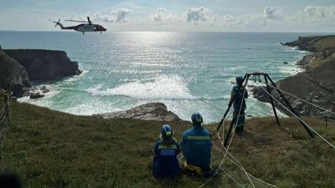 Members of a rescue team on top of a cliff. A helicopter is flying above them. 