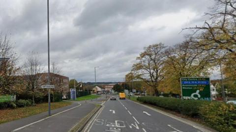 A Google Maps view of a dual carriageway. It runs through a built up area, with industrial units visible on the left.