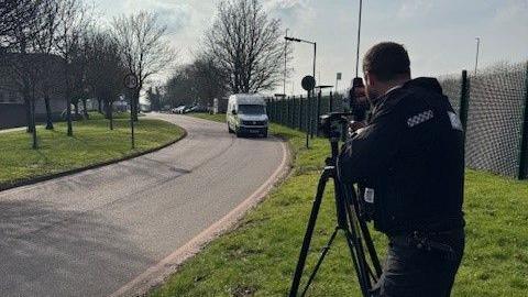 A police officer with a speed camera on a tripod pointed at a road