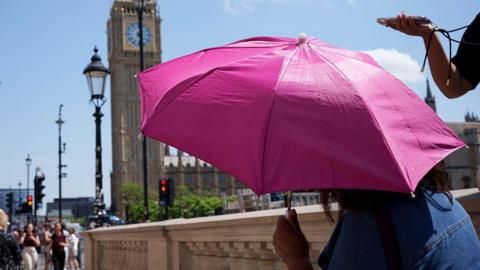 A person shielding from the Sun under an umbrella with the Houses of Parliament in the background