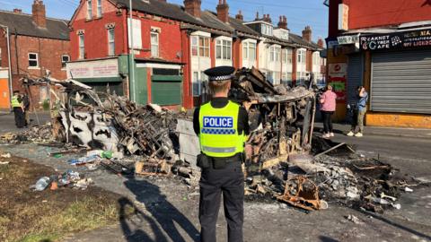 A police officer stands guard over a bus which was burnt out during the trouble in Harehills last year.