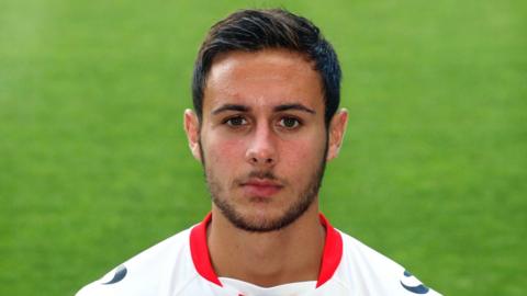 A close-up of George Baldock who has short brown hair and a short brown beard. He is wearing an MK Dons kit.