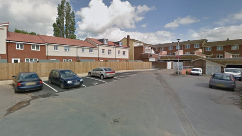A screenshot from Google Street View showing the car park where police say the assault took place. There are several parking bays and indoor garages, tucked behind a row of brick houses.