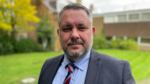 Former Conservative council leader Jason Smithers standing outside in a suit and chequered tie. 