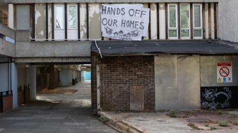 'Hands off our homes' and 'Peabody houses nobody signs' on a derelict housing estate with boarded up entrances