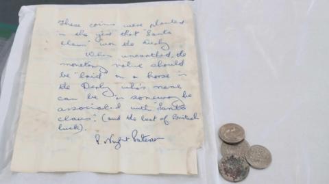 Four coins and a hand-written letter, which says: "These coins were planted in the year that 'Santa Claus' won the Derby. When unearthed, the monetary value should be 'laid on a horse in teh Derby whose name can be in some way associated with 'Santa Claus' (and the best of British luck)