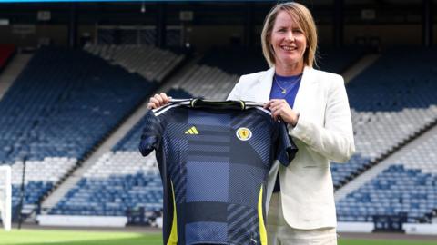 New Scotland head coach Melissa Andreatta in a white suit holding a Scotland top.