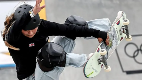 British skateboarder Sky Brown midway through a jump at the Paris Olympics, holding on to her board with one arm in the air