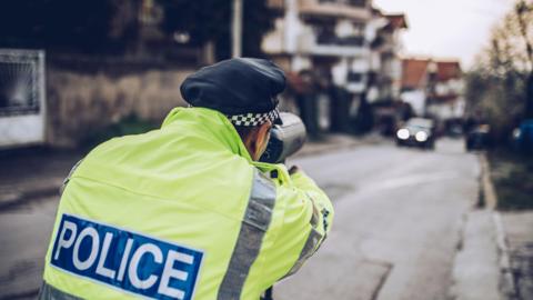 A PSNI officer with a speeding gun pointed at an oncoming vehicle. 