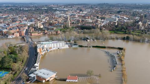 An aerial view shows the cricket ground is pictured under brown water, with rugby posts popping up above the water line next to it and the backdrop of the town of Worcester, taken on Monday.