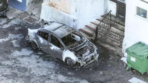 A shot of a burnt out car in front of a mosque