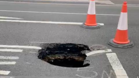 A sinkhole in the centre of the image which has opened up on a concrete road