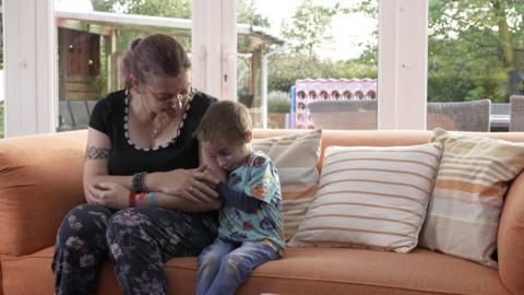 Michaela Middleton sat on the sofa staring down at her son Finley who is hugging on to her arm.