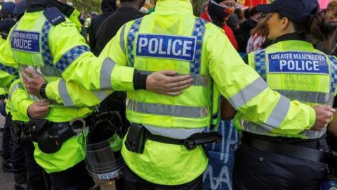 Officers from Greater Manchester Police link arms as they hold people back during disorder in Manchester.