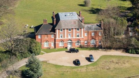 An aerial shot of Forest Lodge in Windsor Great Park, showing a large redbrick country manor house with pillars and cars parked out the front.