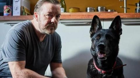 Ricky Gervais with an German shepherd dog in a room from his Netflix series After Life