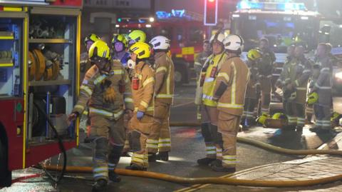 A group of 14 firefighters standing beside a fire engine, at the scene of a fire in Bognor Regis.