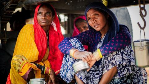 Shanti Devi (L) and her road worker friends crouch beneath a water tanker on a highway bridge over the Ken river