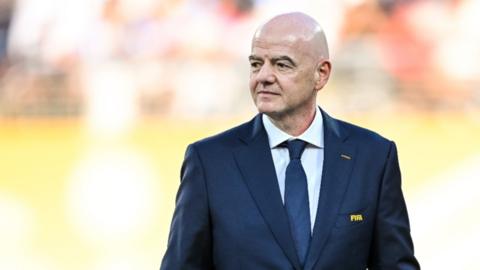 Gianni Infantino wearing a navy blue suit and tie. The Fifa logo is written in yellow on his suit pocket.