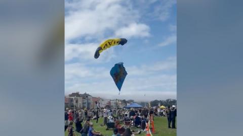 A parachute with a flag descends just above a crowd.